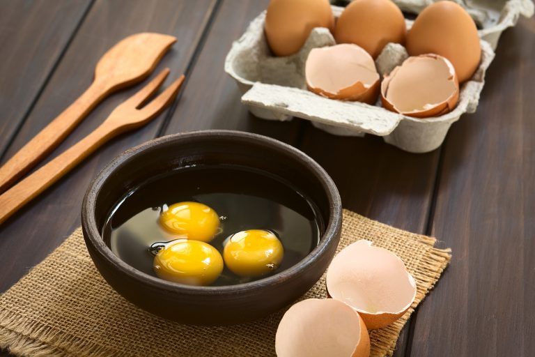 Three raw eggs in rustic bowl with egg box