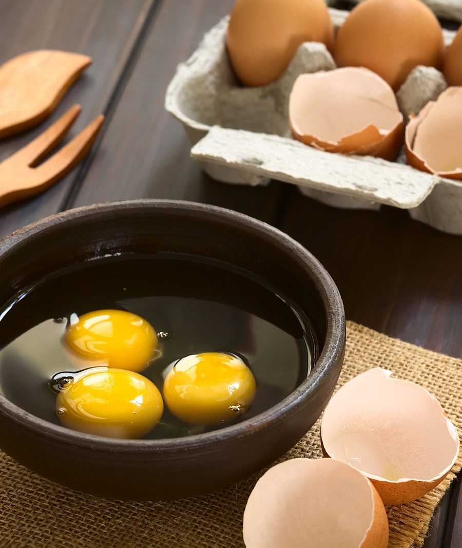 Three raw eggs in rustic bowl with egg box