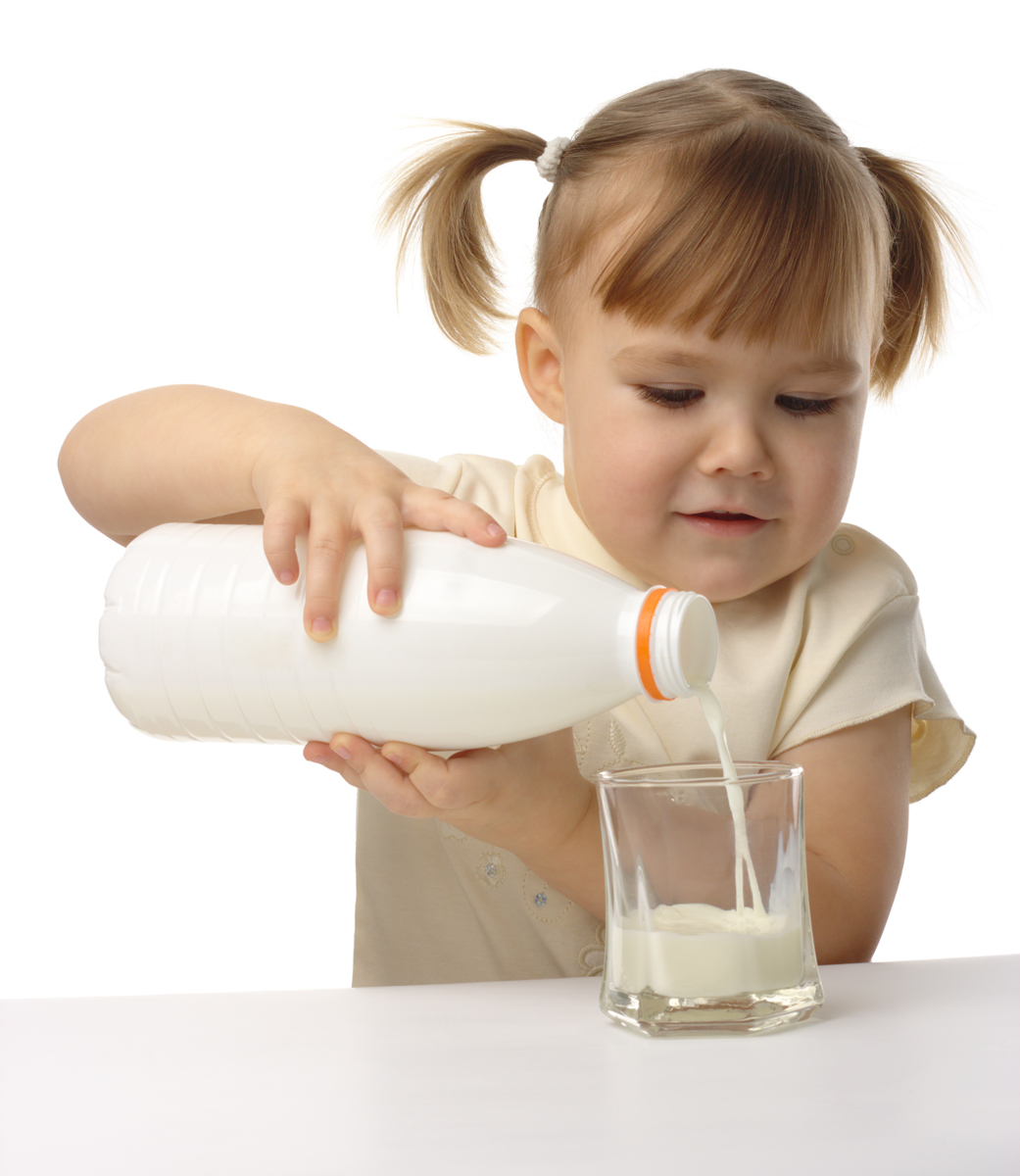 Cute little girl pouring milk in glass, isolated over white