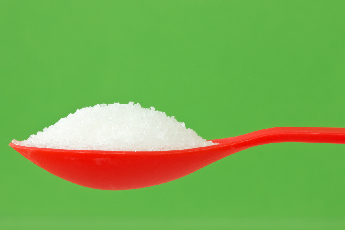 red spoon with sugar isolated on green background