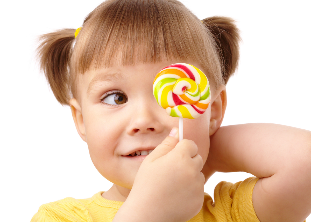 Cute little girl is looking at her colorful lollipop, isolated over white