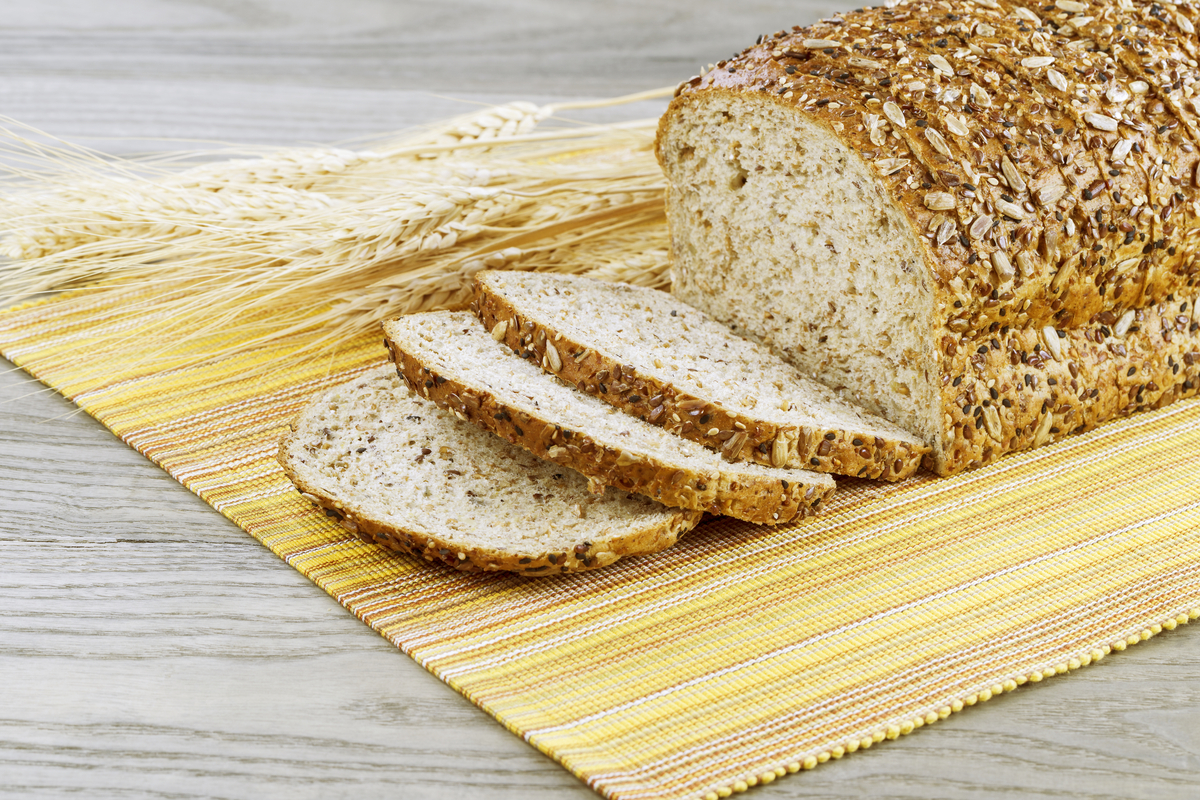 Fresh sliced whole bread with wheat stalks, yellow cloth place mat on faded wooden table