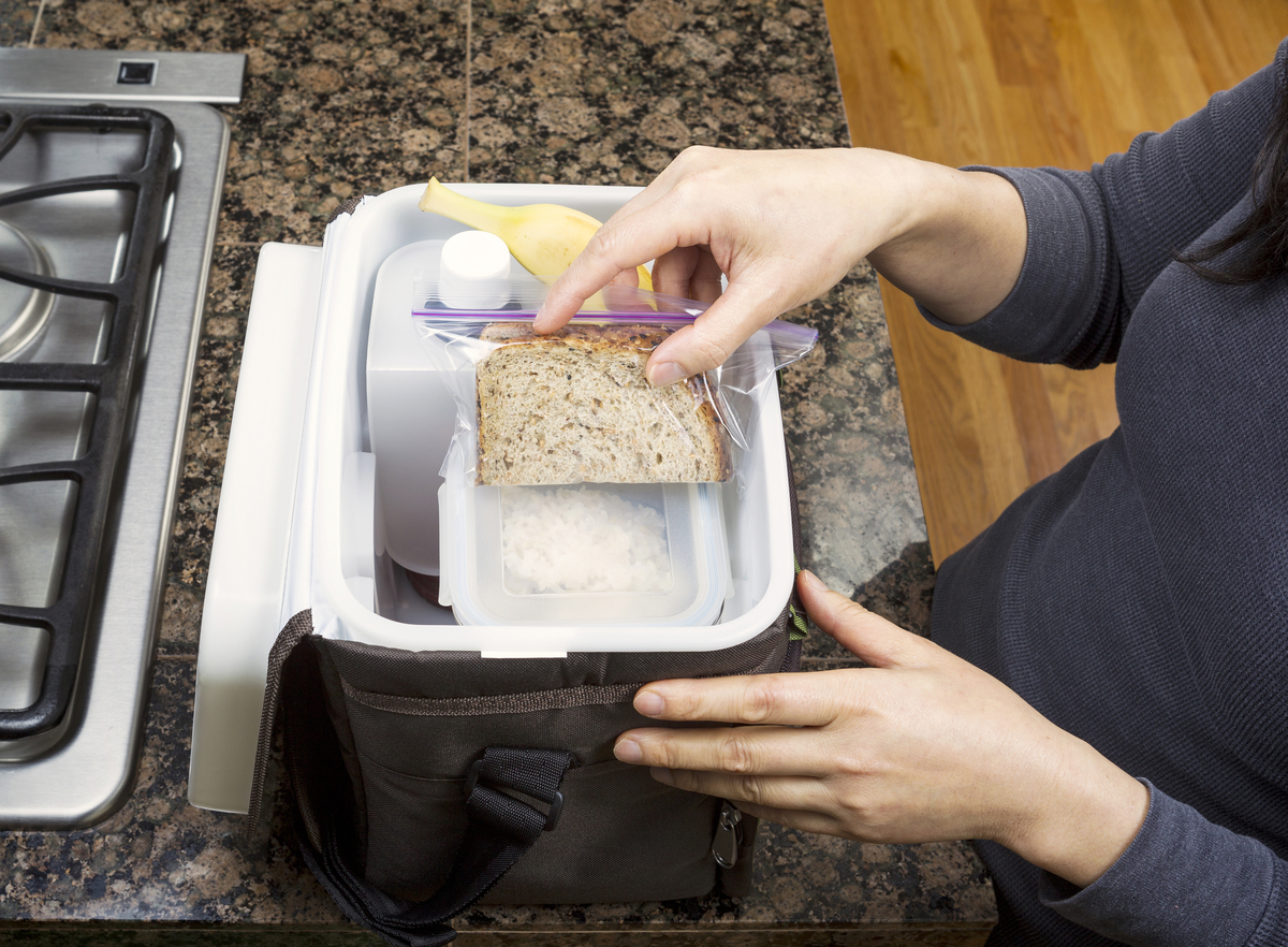 Female hands packing lunch into portable bag while in the kitchen on stone counter top next to stove