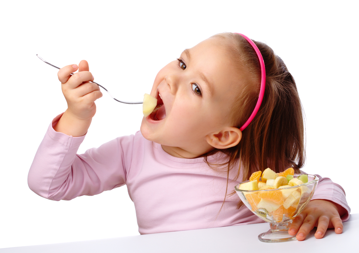 Cute little girl eats fruit salad using fork, isolated over white